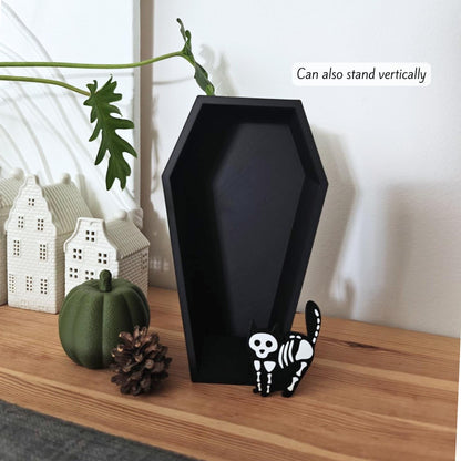 Coffin dish standing vertically on a wooden shelf beside a white house decoration and a small pumpkin, showing alternative display option.