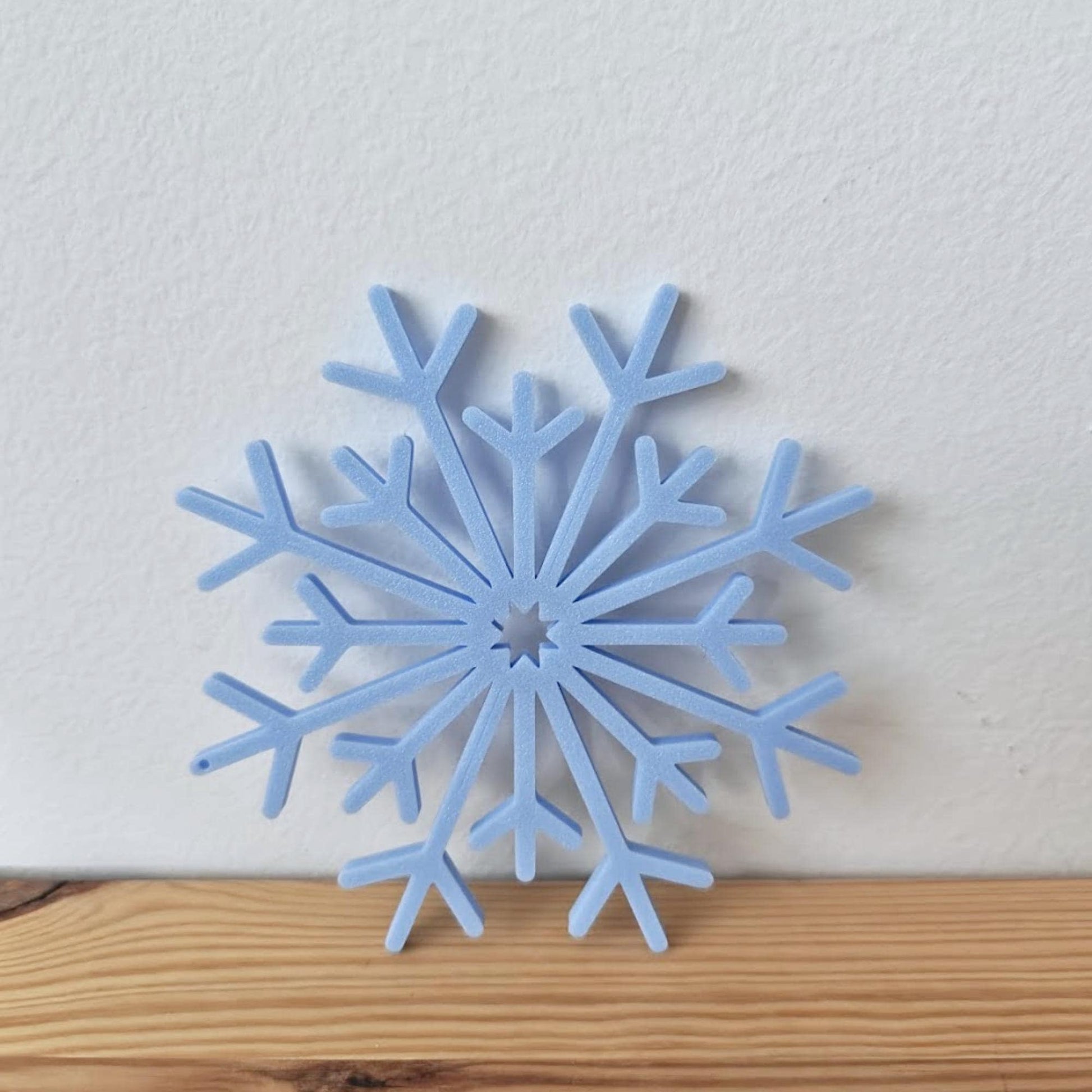 Close-up of a blue 3D-printed snowflake ornament placed on a wooden surface.
