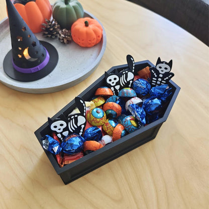 Close-up top view of coffin bowl filled with blue and orange candies, surrounded by pumpkins and Halloween decorations.