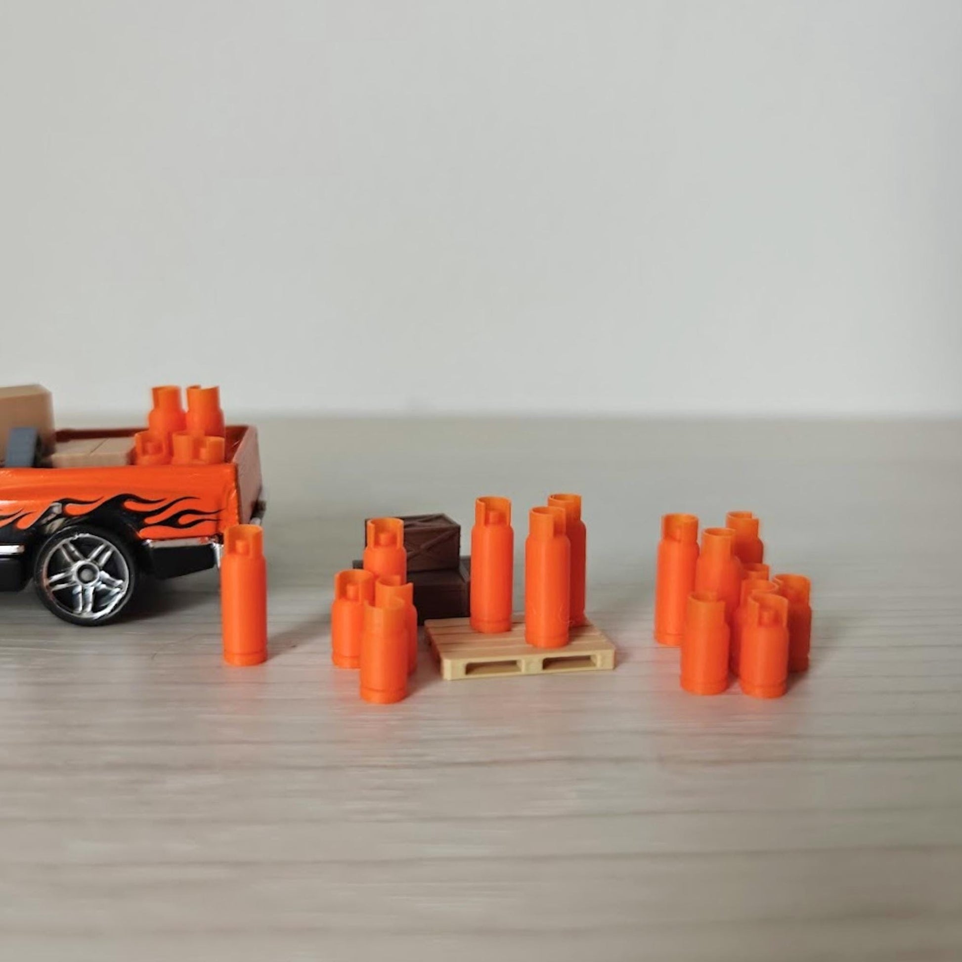 Mixed group of 1:64 scale orange gas bottles with different heights placed near a miniature truck, viewed from an angle.