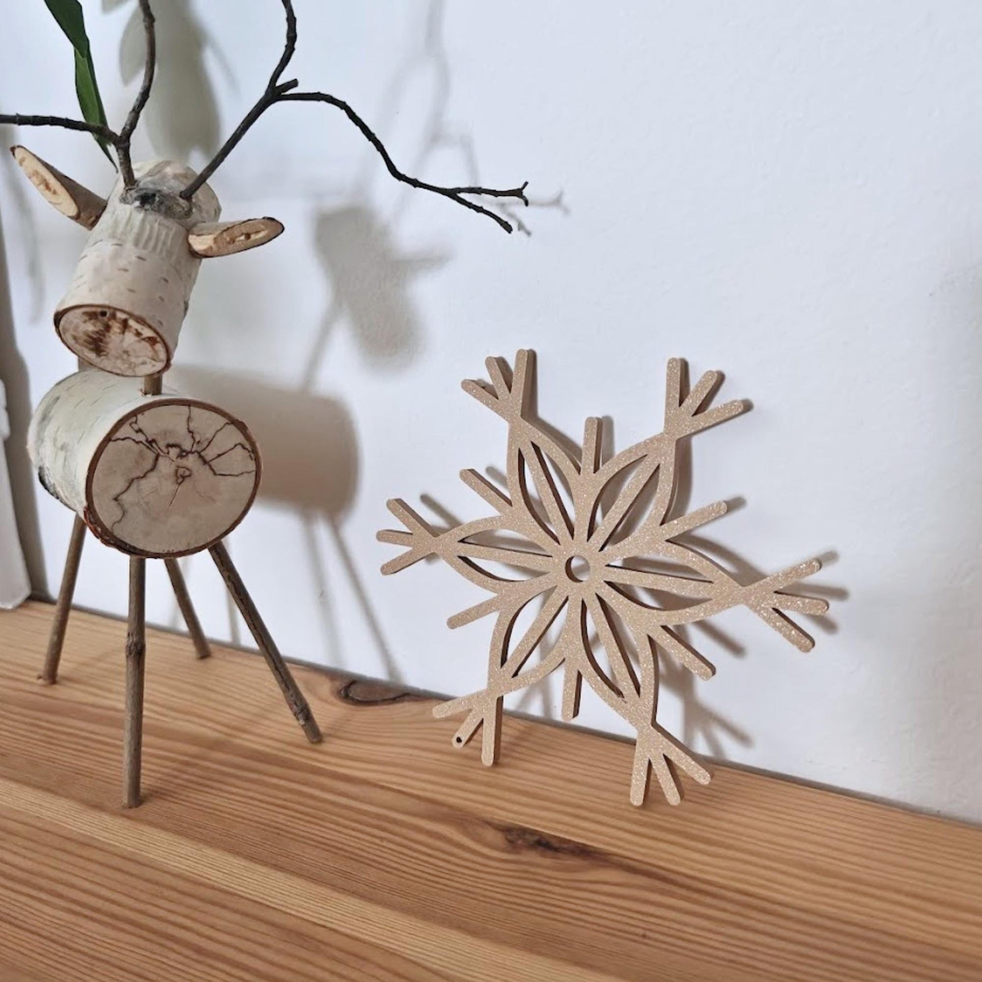 LLatte brown snowflake ornament leaning against a wall, next to Christmas decor.
