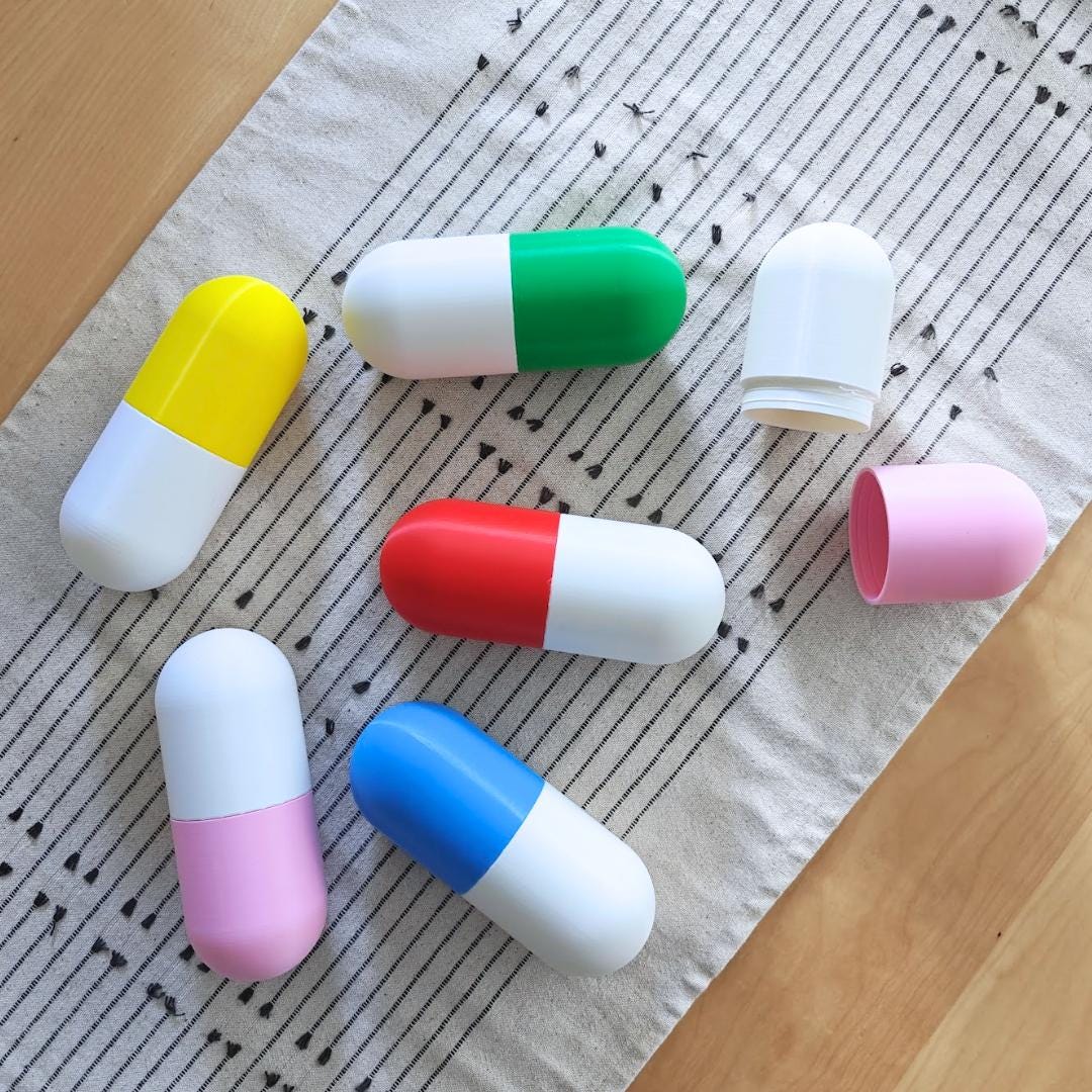 Assorted colorful pill-shaped gift boxes displayed open and closed, designed for candy, tiny treasures or secret messages.