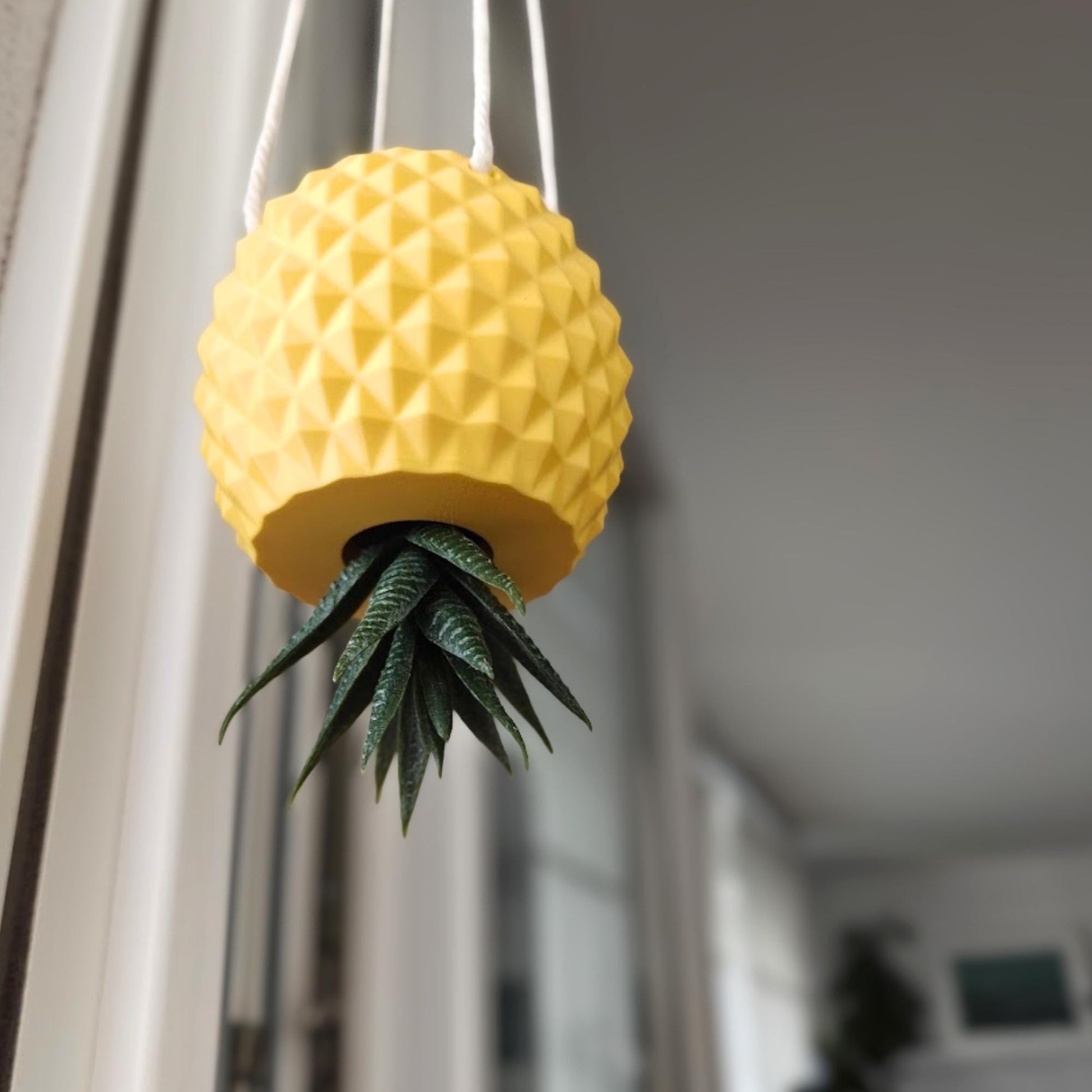 Hanging inverted pineapple planter with plant extending through bottom opening