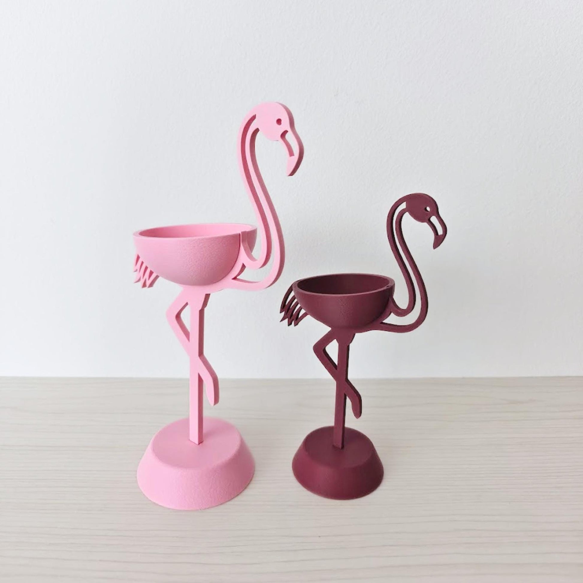 Pink and burgundy flamingo plant holders without plants on neutral background