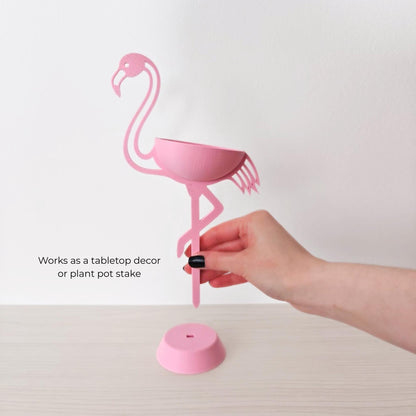 Hand holding flamingo plant holder showing removable base and stake use