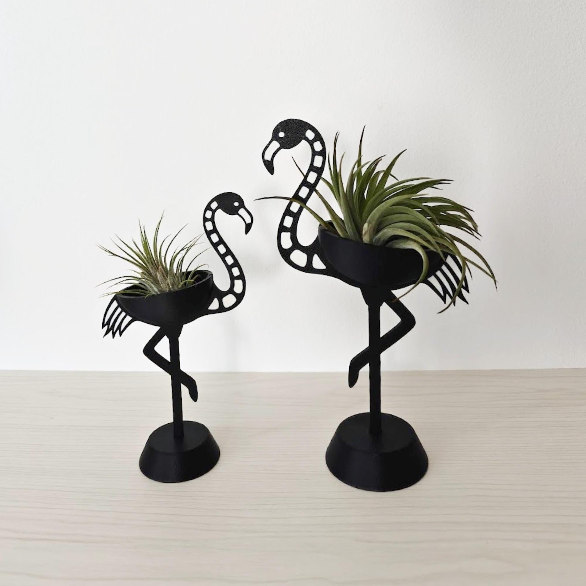 Two skeleton flamingo air plant holders in black, small and large size, placed on a light surface