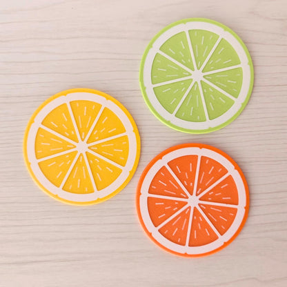 Lemon, lime and orange fruit slice coasters arranged on a light wood surface.