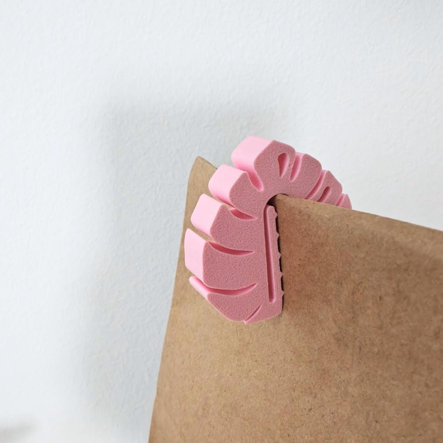 Pink monstera leaf bag clip closing the top of a brown paper lunch bag.