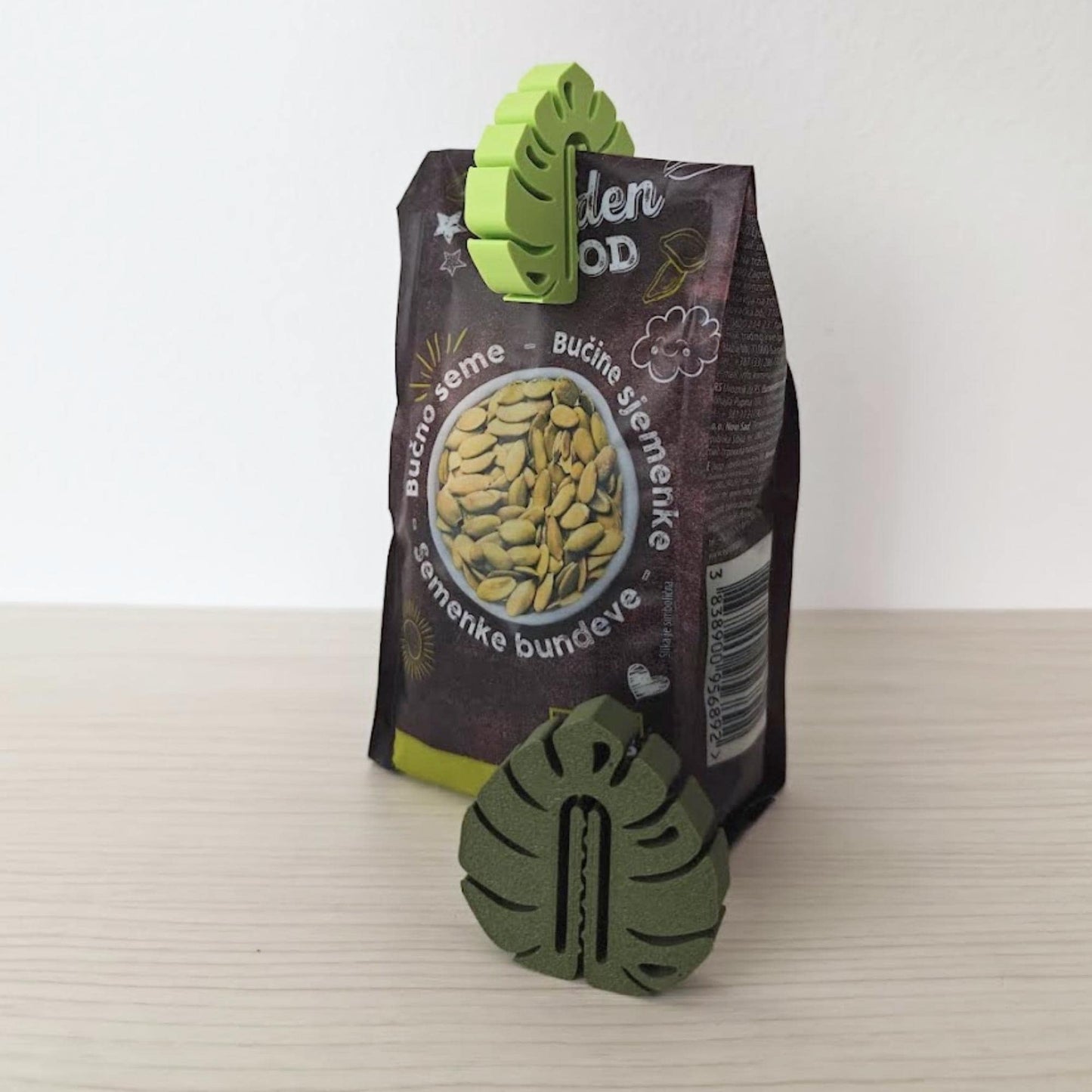 Green monstera leaf clips sealing a small snack bag on a light tabletop.