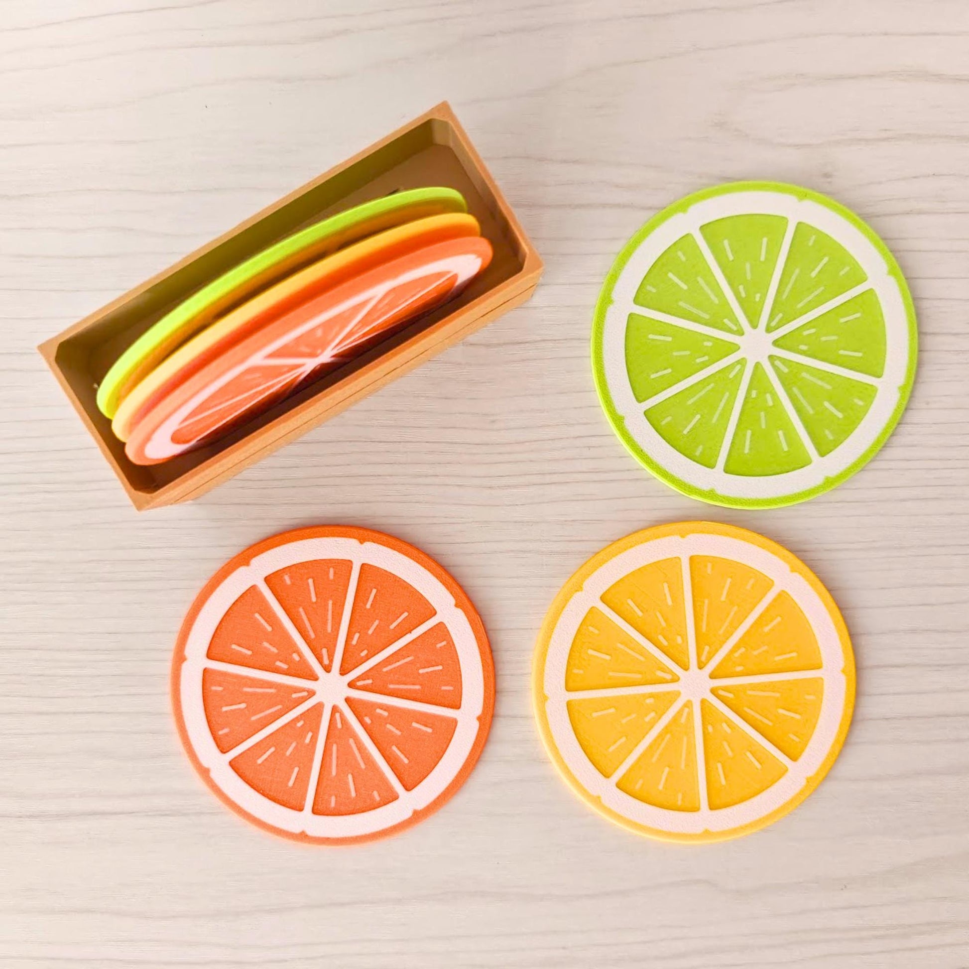 Six citrus slice coasters in lemon, orange and lime colors displayed beside a wooden crate holder.