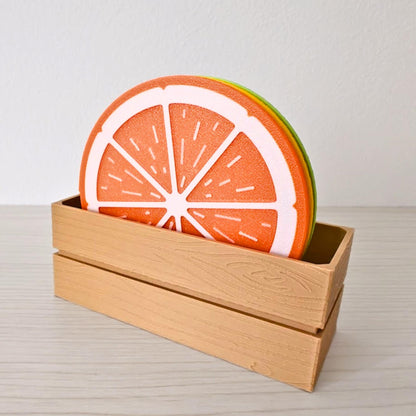 Orange slice coaster standing in a wooden crate holder with lemon and lime coasters stacked behind it.