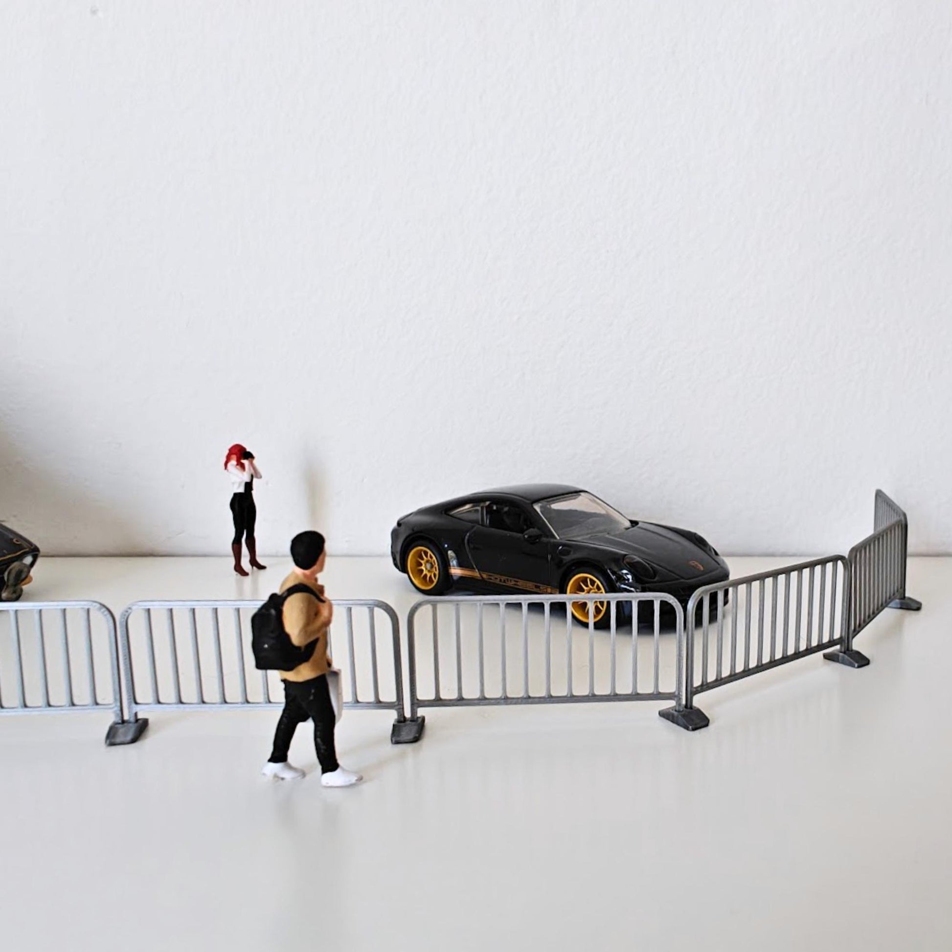 Small silver crowd control barriers arranged in a curved street diorama scene with a car and miniature figure.