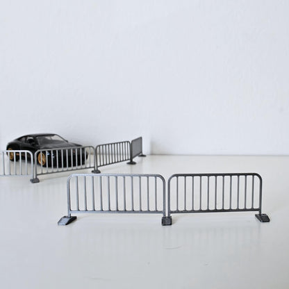 Two assembled miniature metal barricades shown from the front with additional barriers and a diecast car in the background.