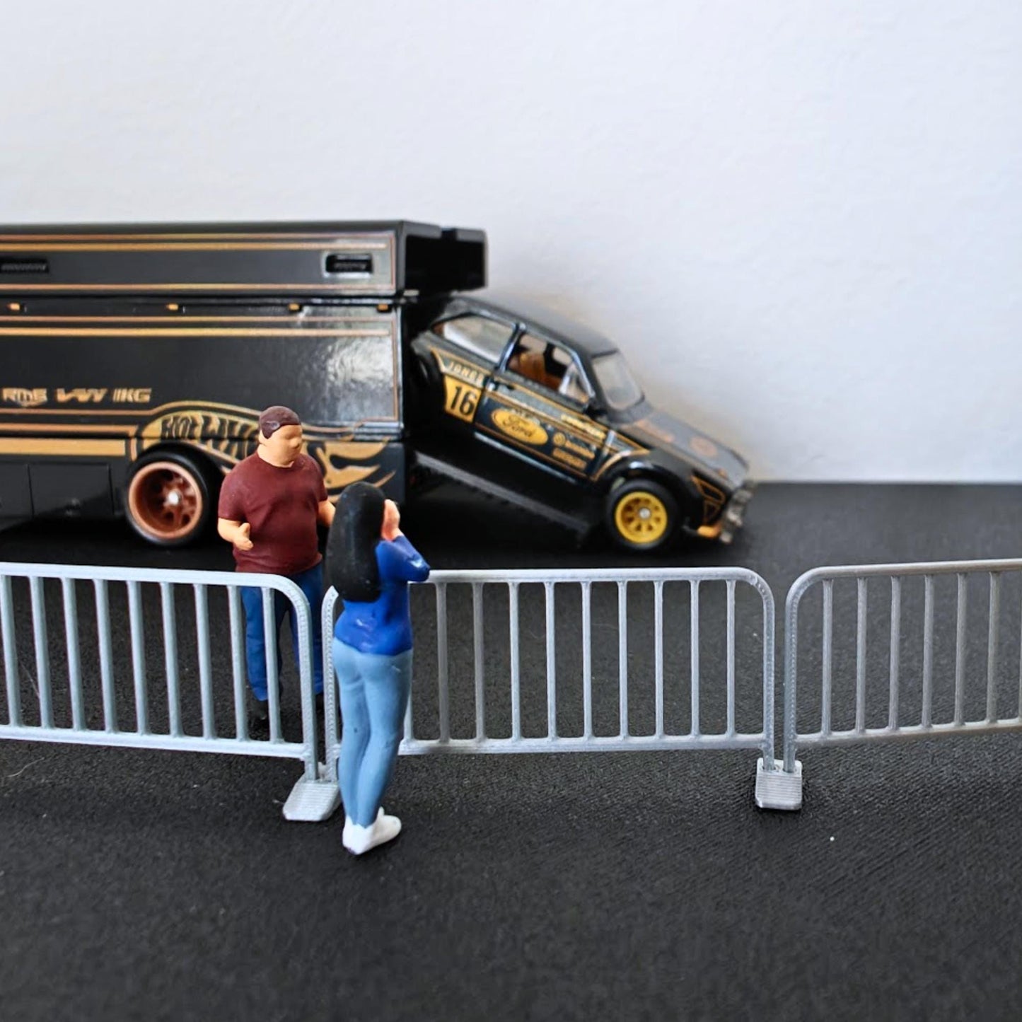 1:64 scale galvanized-style barricades placed in front of a black diecast vehicle and small model figures.
