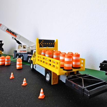 Yellow model construction truck carrying miniature orange traffic barrels with white bands.