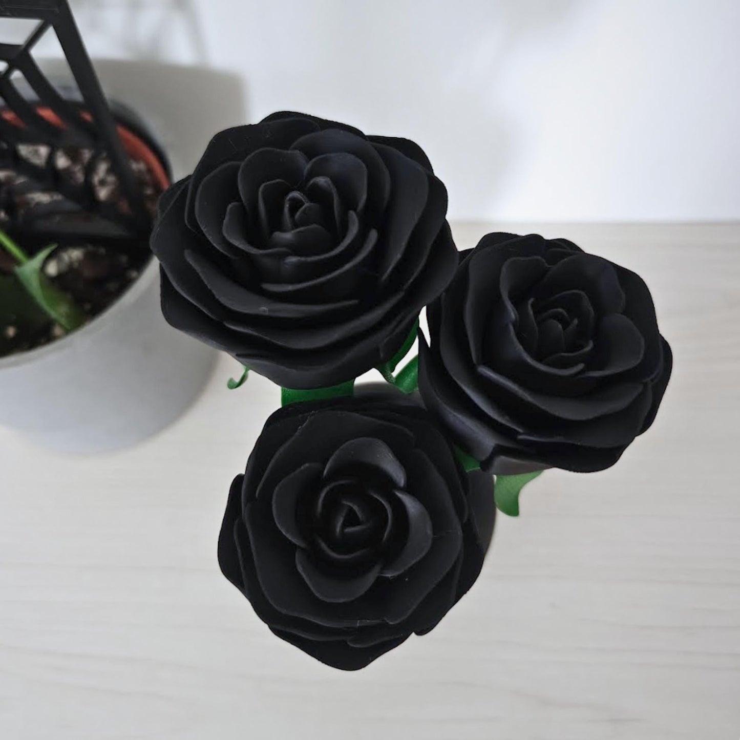 Close-up top view of three matte black artificial roses with layered petals and green stems.