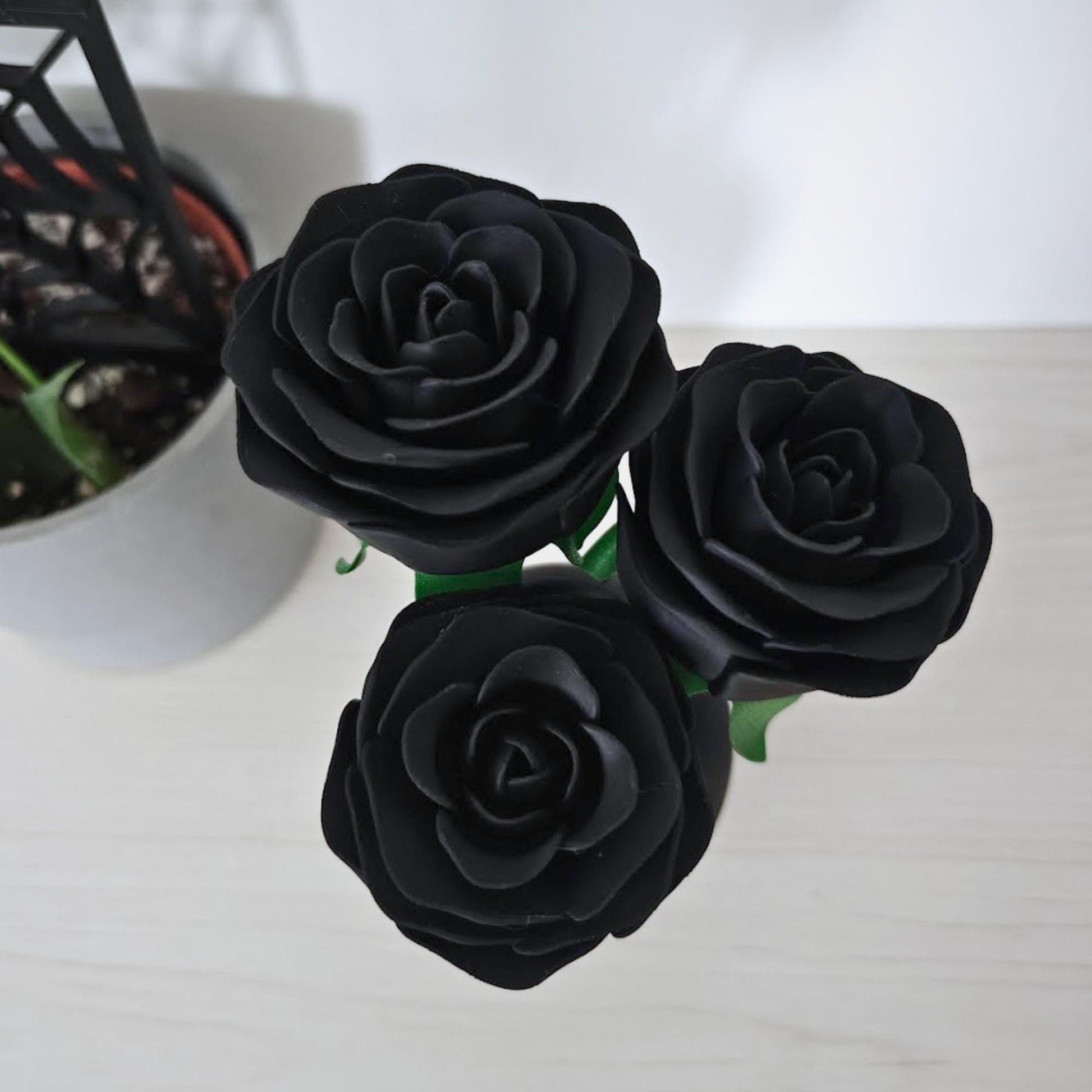 Close-up top view of three matte black artificial roses with layered petals and green stems.