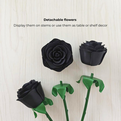 Detachable black rose heads shown separately from their green stems and leaf-shaped bases on a light wood background.