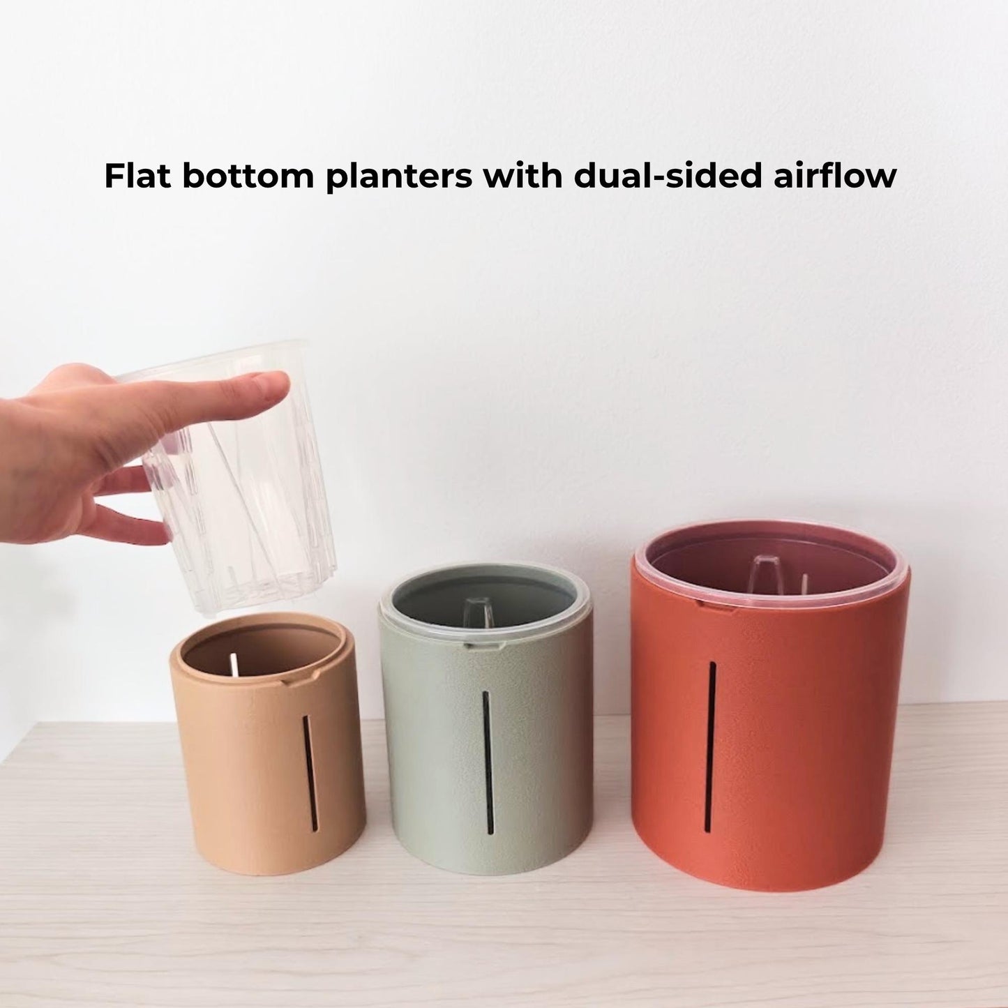 Hand lifting a clear nursery pot above three flat-bottom planter covers with dual-sided airflow openings.