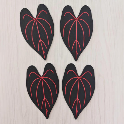Four black Anthurium Queen of Hearts leaf coasters with bright red veins laid flat on a light wooden surface.