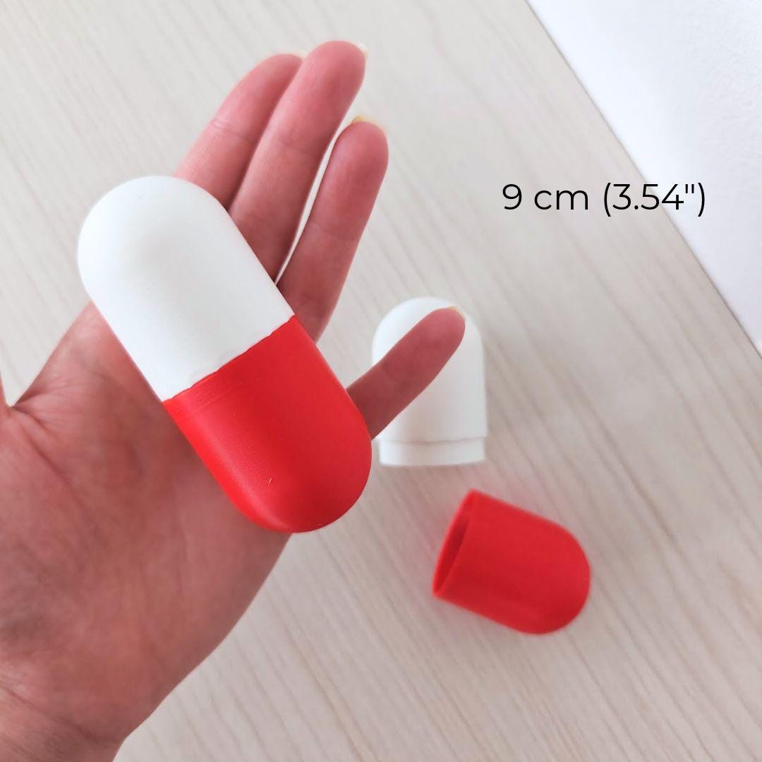 9 cm red and white pill capsule box held in one hand with the removable lid beside it, suitable for tiny gifts or messages.