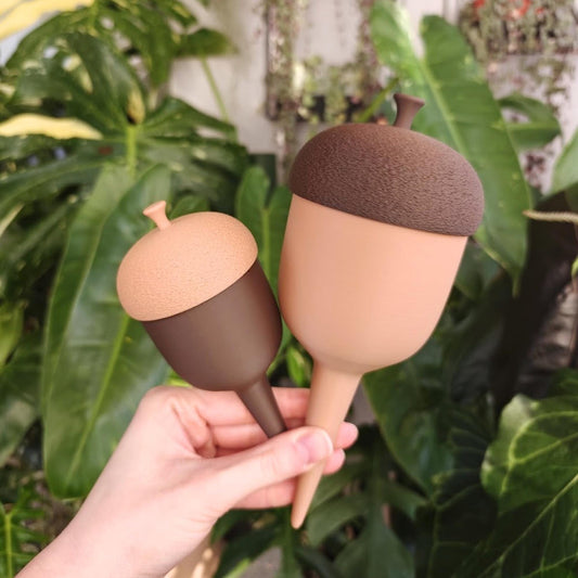 Small and large acorn-shaped plant watering spikes held together in front of tropical houseplants.