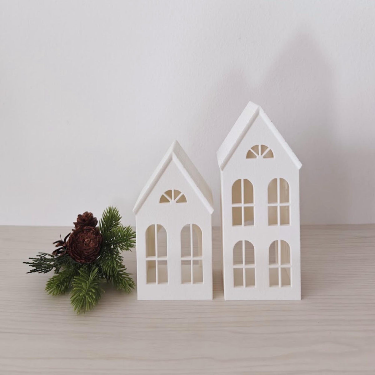 Two white decorative house tealight holders with winter greenery
