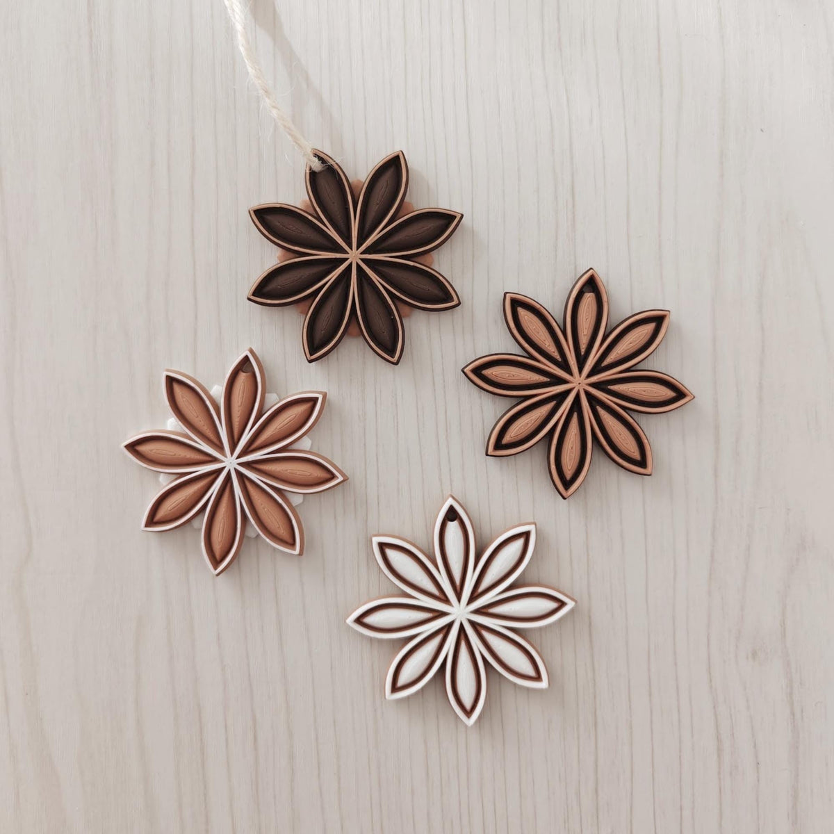 Set of star anise hanging ornaments in mixed brown, white and natural tones on a light wood background.